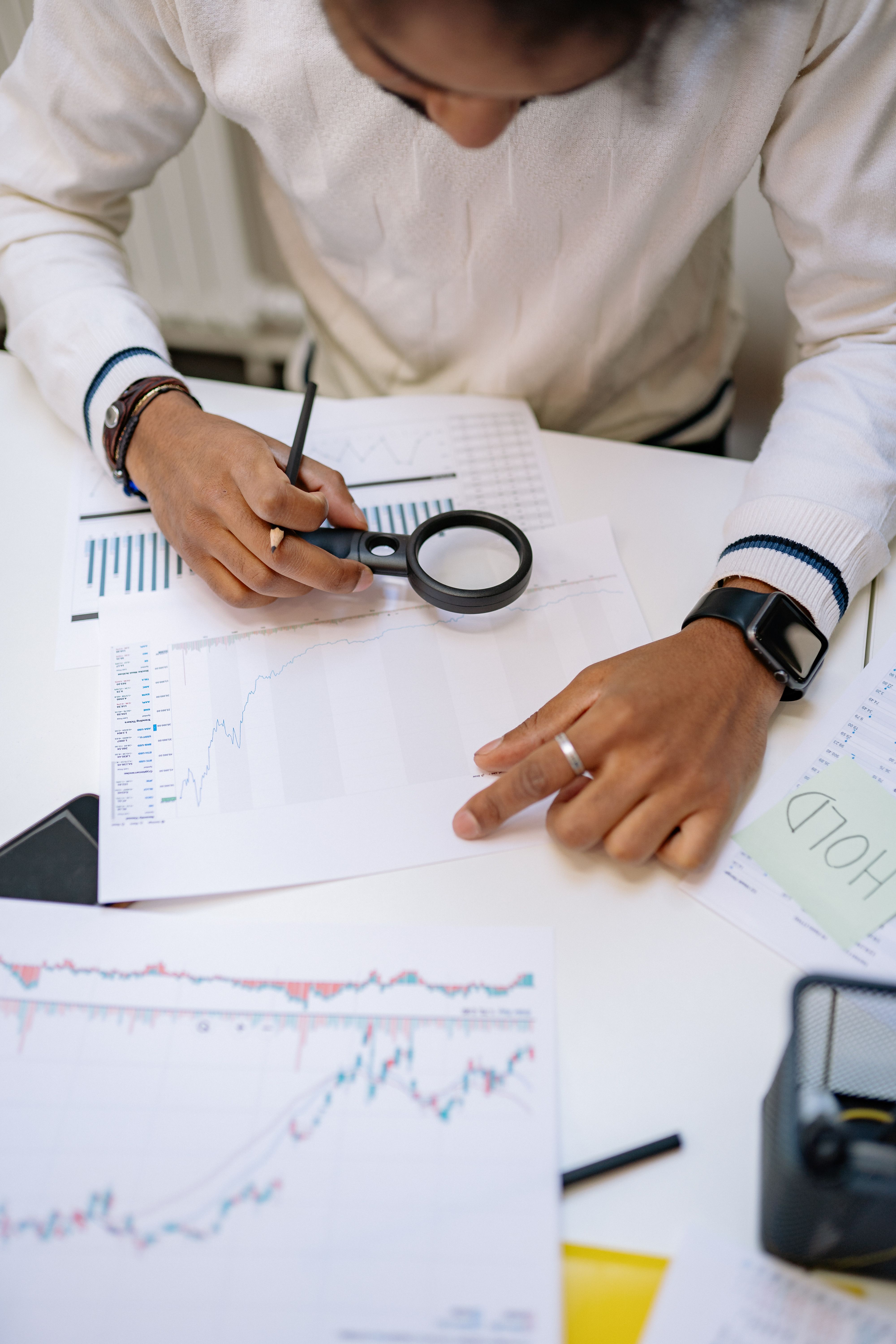Analista revisando gráficas impresas con lupa y lápiz sobre una mesa de trabajo